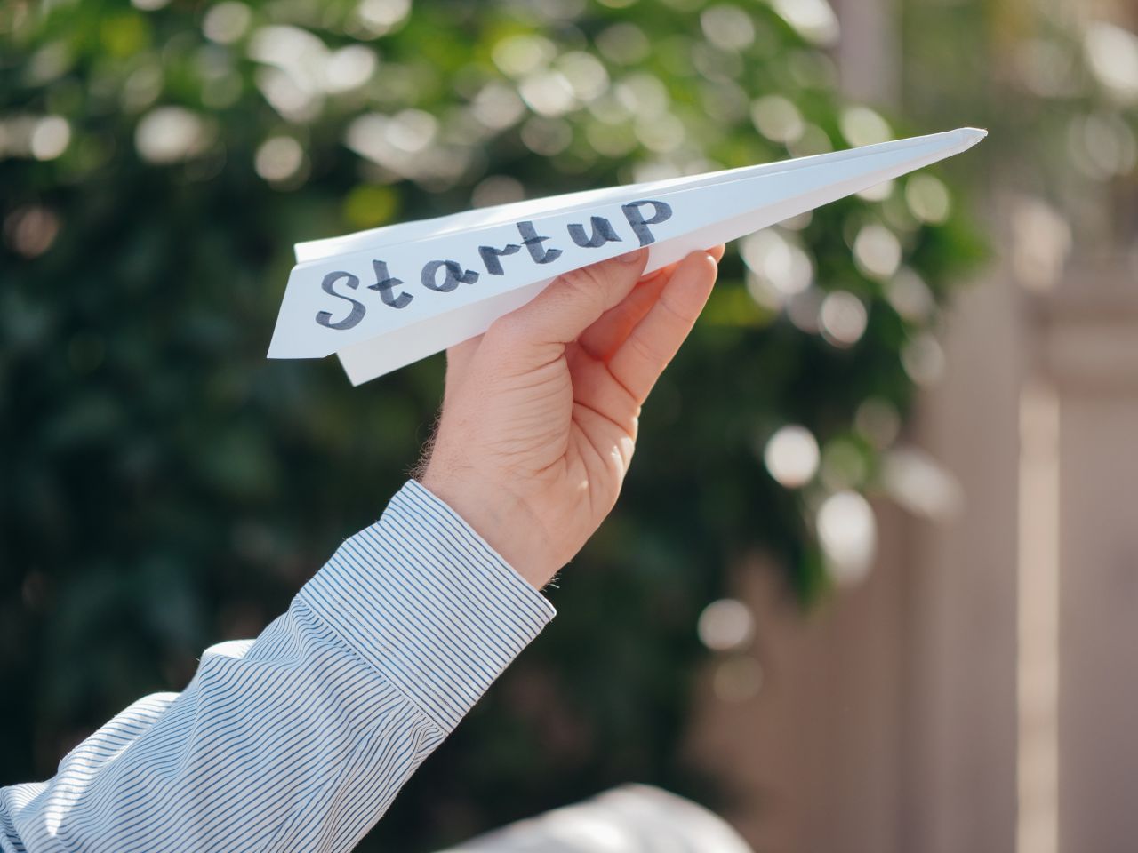 services-02 Gros plan sur une main tenant un avion en papier portant le mot Startup, symbolisant le lancement d’une entreprise.